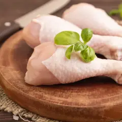 Trois cuisses de poulet cru sur une planche en bois, garnies de basilic. Un couteau est visible en arrière-plan. Mon chien adore le poulet cru.